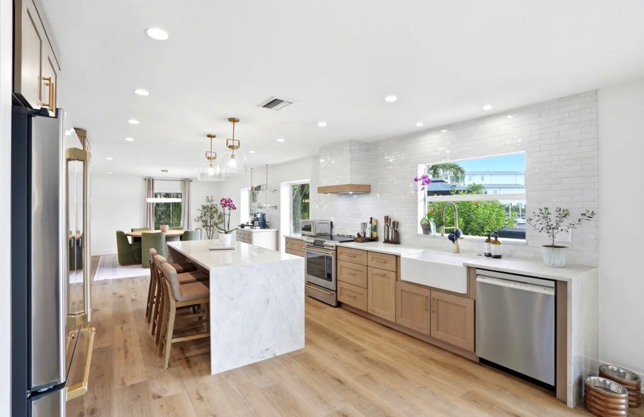White oak kitchen with a marble waterfall island, farmhouse sink and brass pendants, open to the dining room