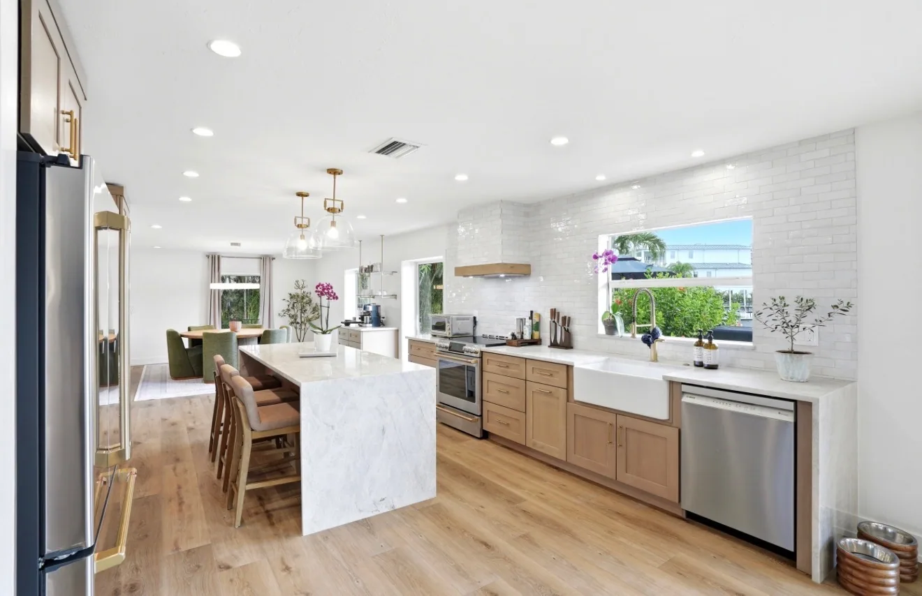 Bright completed kitchen with natural wood cabinetry, a waterfall island, and white tile walls