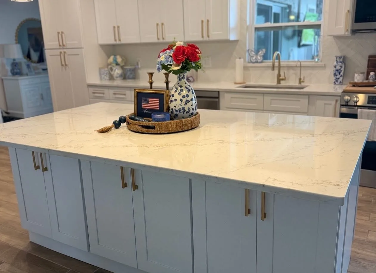 Kitchen with pale blue-grey cabinetry, a cream stone counter and brass bar pulls