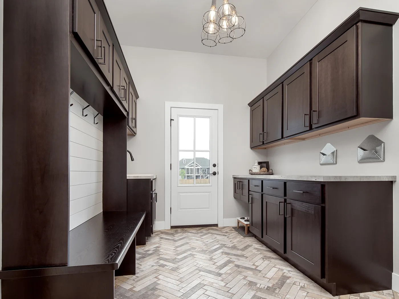 Built-in storage wall in a mudroom, with a hanging rail and hooks above a bench, closed upper cabinets and a run of drawers opposite
