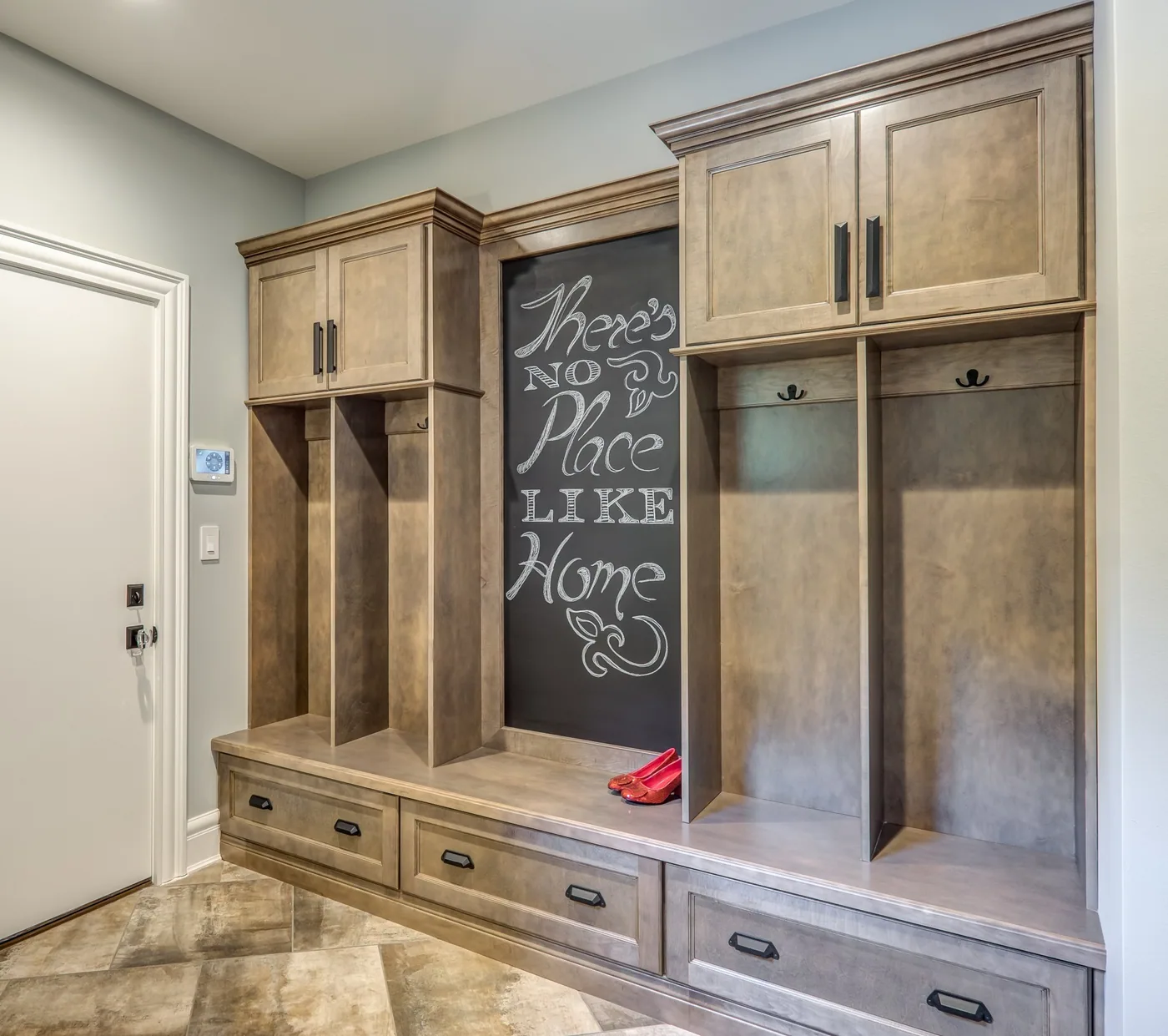 Mudroom cabinetry in warm gray stained wood, with tall lockers, cubbies, bench seating and drawers, from Wellborn Forest